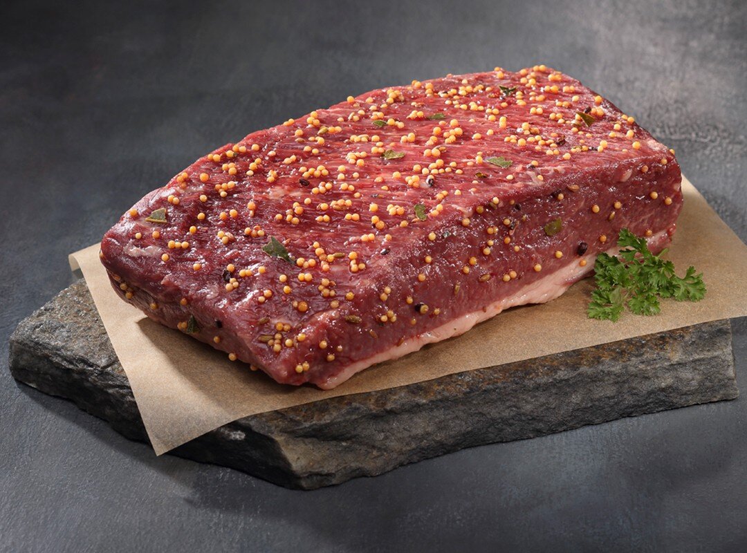 Kat+-+Corned+beef+brisket Juicy, medium-rare steak being sliced on a wooden cutting board, showcasing its tender pink interior and seared crust, with a carving knife and fork positioned for serving.