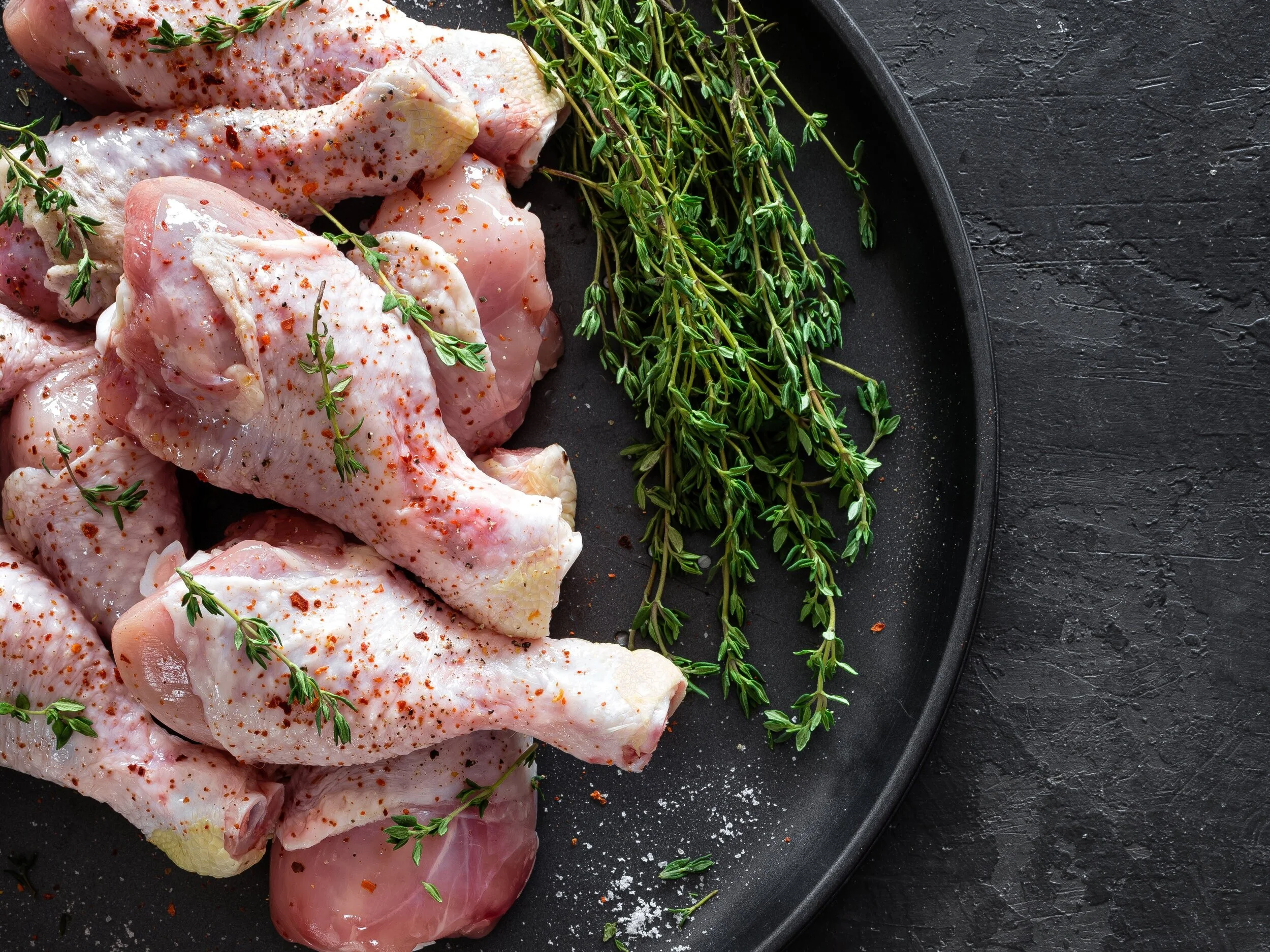 Raw+marinated+chicken+meat+chicken+legs+ Succulent pulled pork on a wooden cutting board, showcasing tender, shredded meat with a crispy outer layer. A fork rests beside the meat, highlighting its juicy texture and rich seasoning.