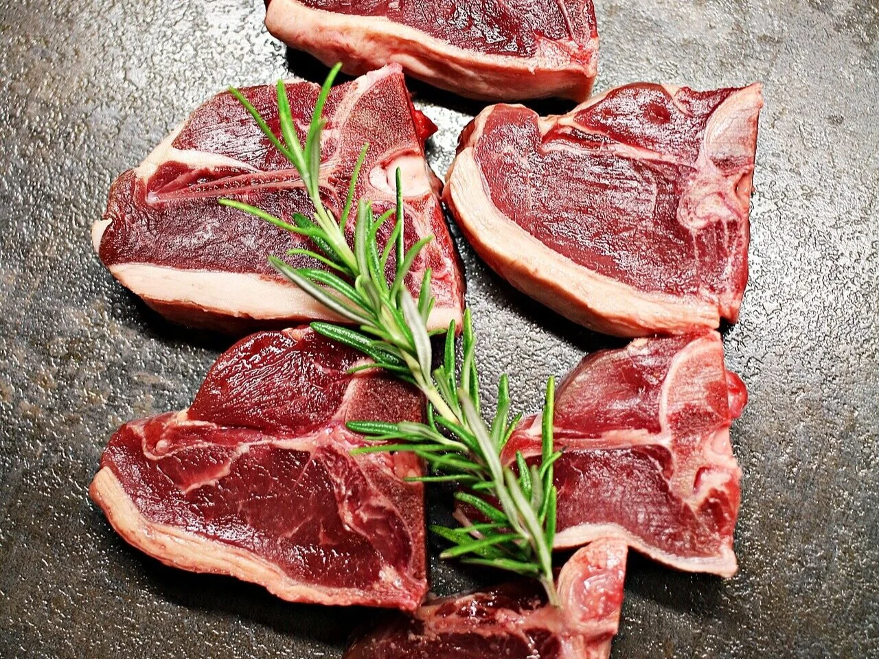 lamb_porterhouse_tbone Juicy, medium-rare steak being sliced on a wooden cutting board, showcasing its tender pink interior and seared crust, with a carving knife and fork positioned for serving.